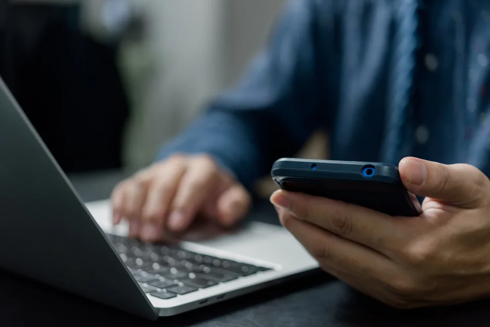 Person using a mobile phone beside a laptop